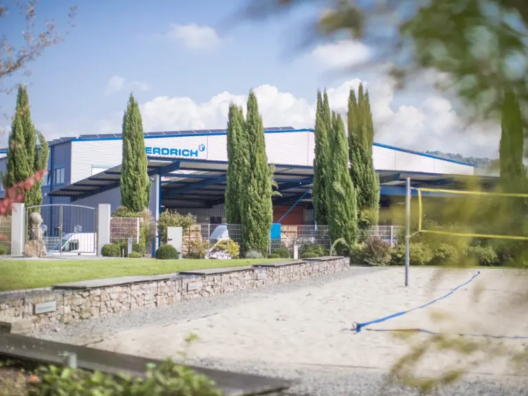 Wiese mit Bäumen im Vordergrund. Im Hintergrund ist das Unternehmensgebäude von Erdrich zu sehen. 