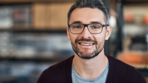 Ein bärtiger Mann mit Brille lächelt nach einem KEFF+Check, der Einsparmöglichkeiten im Unternehmen offengelegt hat.